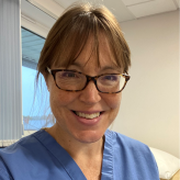 A photo of Dr Nicola Wray, wearing glasses and medical scrubs.