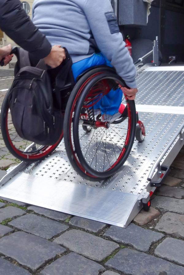 A healthcare worker pushing a wheelchair up a ramp and into a car.