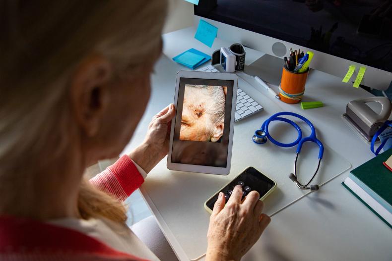 A GP holding a video call appointment and looking at a wound on a tablet screen.