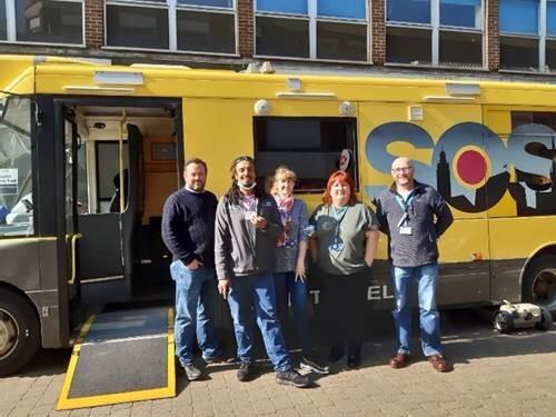 People standing in front of a yellow bus displaying the word 'SOS'